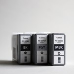 Photograph of three Canon printer cartridges standing upright on a grey background