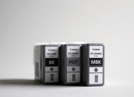 Photograph of three Canon printer cartridges standing upright on a grey background