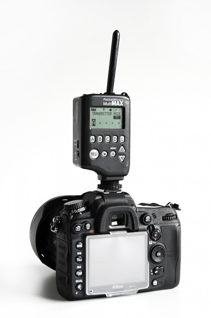A Nikon D7000 is shown with a Pocket Wizard radio transmitter attached to the camera's hot shoe.