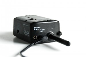 A Pocket Wizard radio transmitter is shown with a flash sync cable plugged into the flash port.