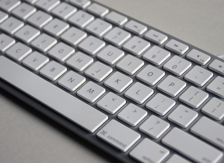 Close up photograph of Apple white and silver keyboard on a grey backdrop.