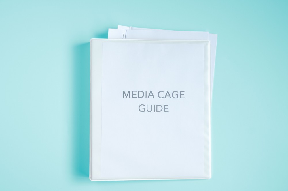 Image of Binder with piece of paper on it that says Media Cage Guide